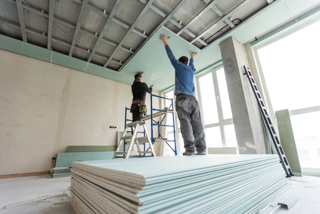 Kosten für Trockenbau wand- Ein Mann der hellblaue Fliesen an der Decke anlegt